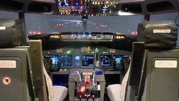 Flugzeugcockpit mit beleuchteter Steuerung und Blick auf die Landebahn.