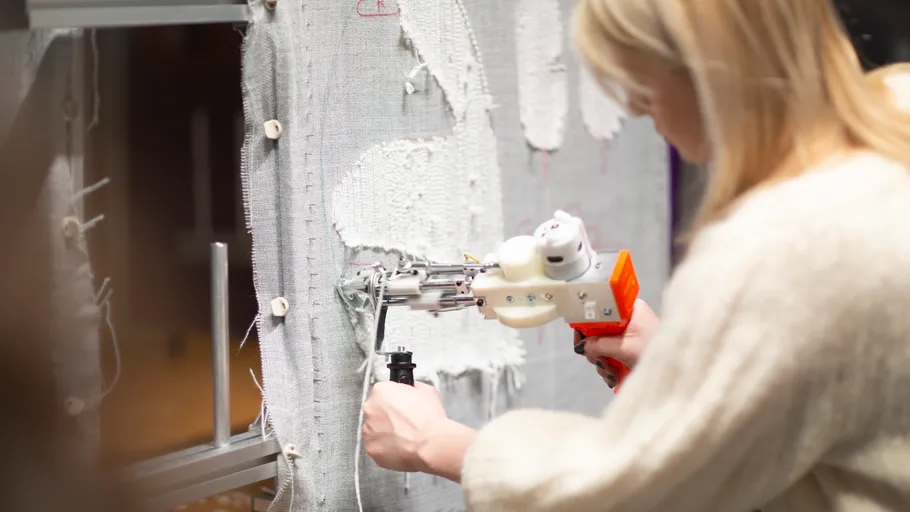 Person using tufting gun on fabric canvas.