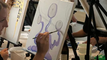 Person painting abstract purple shapes on canvas.