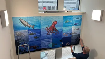 Die Person installiert ein Wandgemälde mit Meeresmotiven an der Wand.