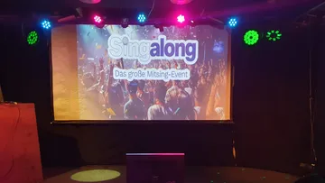Projector screen displaying 'Singalong' event promotion.
