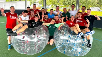 Group of men posing with bubble soccer balls on a field.