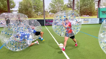 People playing bubble soccer on artificial turf.