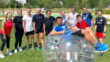 Group of people outdoors around clear bubble object.