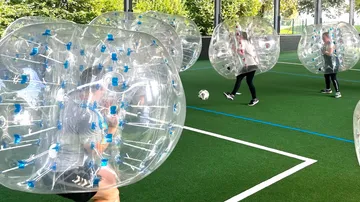 Leute spielen Bubble Soccer auf einem Rasenfeld.