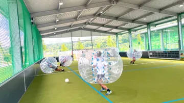 Leute spielen Bubble Soccer drinnen auf Rasen.