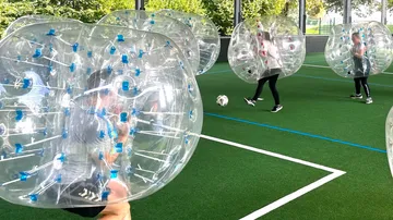 Leute, die Bubble Soccer auf einem Hallenfeld spielen.