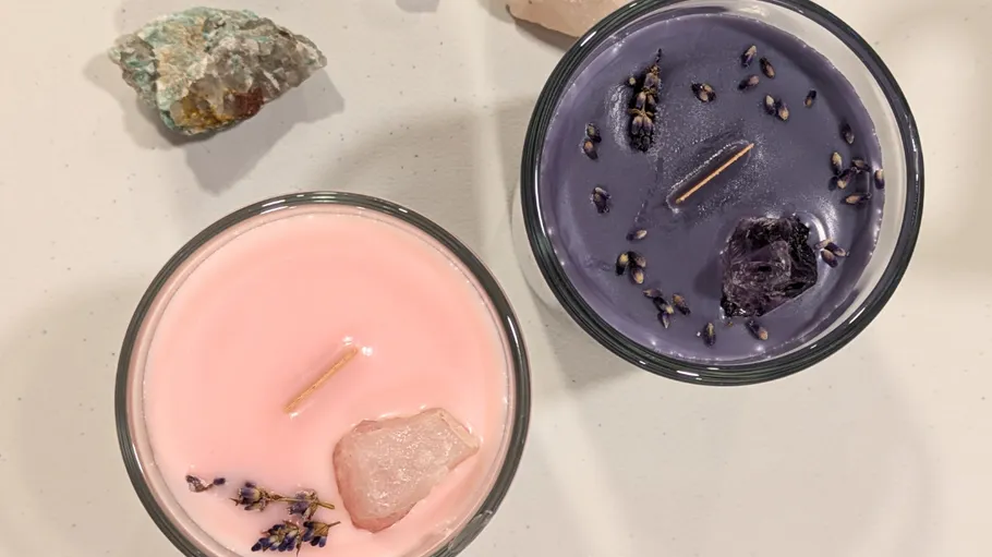 Two candles with crystals and plants on table.
