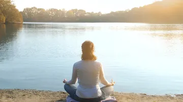 Person, die an einem ruhigen See meditiert.