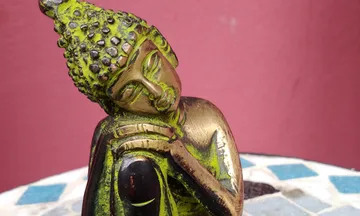 Buddha-Statue mit grüner Oberfläche, rosafarbenem Hintergrund.