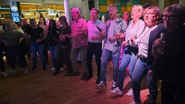 Group of people singing and dancing at bar.