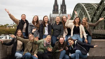 Gruppe von elf Personen, die draußen in der Nähe einer Brücke und einer Kathedrale lächeln.