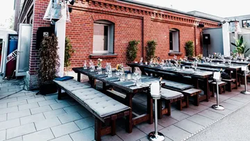 Outdoor dining setup with long tables against brick wall.