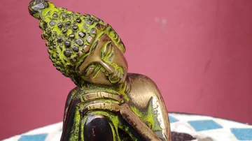Buddha-Statue mit geschlossenen Augen, rosafarbener Hintergrund.