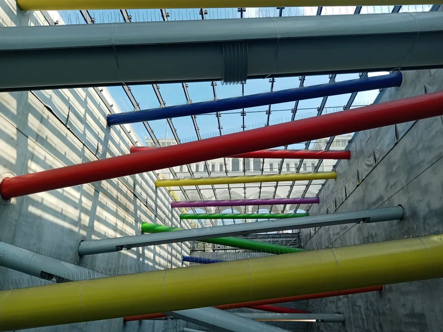 Colourful pipes hang diagonally over a concreted room.