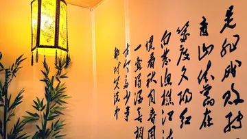 Die Lampe im asiatischen Stil beleuchtet die Kalligrafie an der Wand.