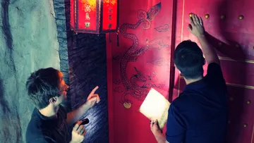 Two people examining a red door with dragon design.