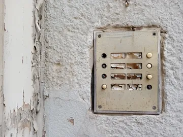 Worn out intercom on a damaged wall.