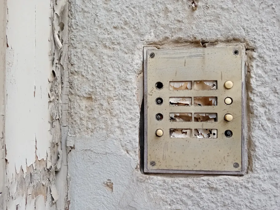 Abgenutzte Gegensprechanlage an einer beschädigten Wand.