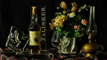 Whiskyflasche, Glas, Laterne und Blumen auf dem Tisch.