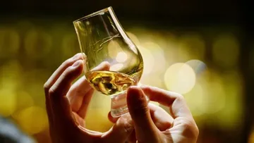 Hands holding a glass of whiskey, blurred background.