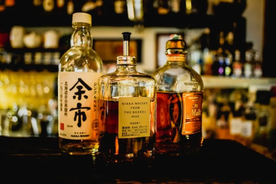 Three whiskey bottles on a bar shelf.