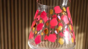 Glas mit bunten Farbpunkten, gestreifter Hintergrund.