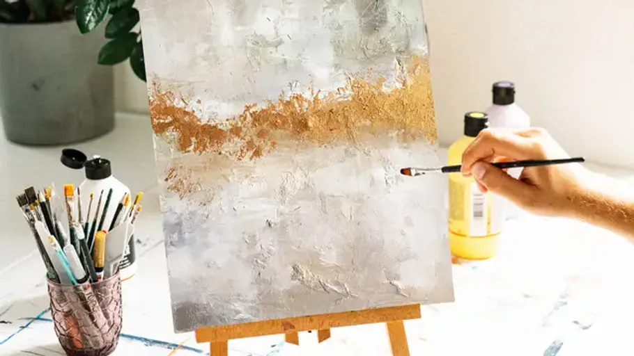 Person painting abstract canvas with brushes on easel.