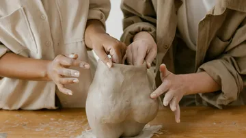 Two people sculpting clay vase on table.
