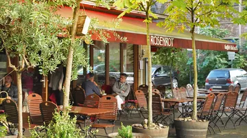 Café-Sitzplätze im Freien unter Bäumen, rote Markise.