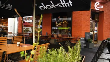 Cafétische im Freien mit orangefarbenem Fassadenhintergrund.