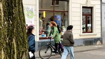 Woman in green coat bicycling on city street.