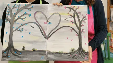 Two people hold twin tree heart painting.