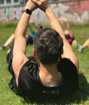 Person exercising on grass outdoors, others in background.