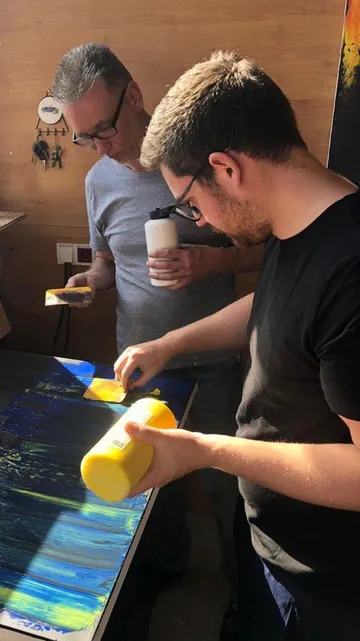 Zwei Männer malen mit Spachteln, bunte Leinwand.