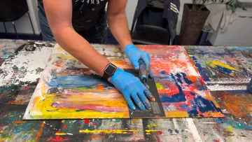 Person applying paint on canvas with spatula.