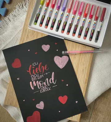 Dekorativer Schriftzug auf schwarzem Papier mit Stiften.