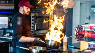 Koch hält eine flammende Pfanne in der Küche.