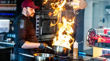 Koch kocht mit flammender Pfanne in der Küche.