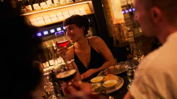 Frau mit Weinglas in einer schwach beleuchteten Bar.