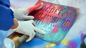 Die Person verwendet eine Schablone mit Sprühfarbe auf Beton.