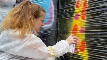 Person, die bunte Graffiti auf Plastikfolie sprüht.