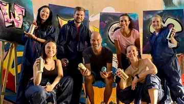 Group posing with spray cans, graffiti background.
