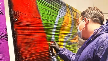 Artist spray-painting vibrant mural on wall.