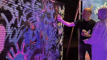 Zwei Künstler sprühen Neongraffiti auf die Wand.