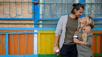 Couple holding coffee cups with colorful background.