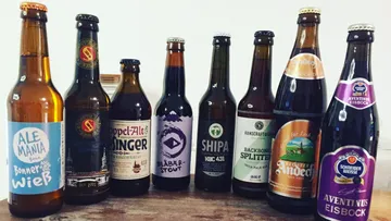Acht verschiedene Bierflaschen, aufgereiht auf dem Tisch.
