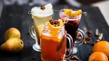 Three mugs of spiced beverages on table.