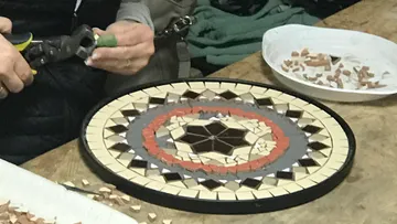 Person, die ein Mosaikmuster mit Werkzeugen auf dem Tisch bastelt.