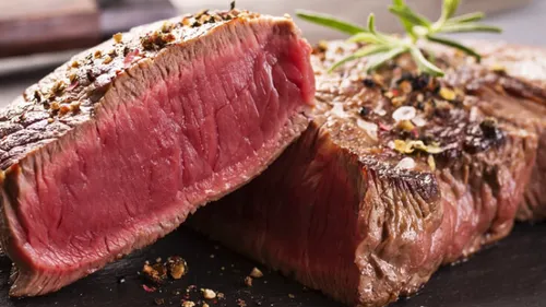 Mittelseltenes Steak, in Scheiben geschnitten auf einem Teller, garniert mit Kräutern.